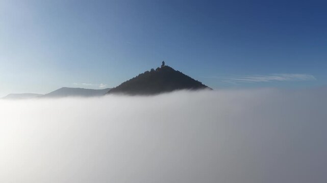 Aerial view of the medieval Haut-Koenigsbourg castle perched atop a mountain piercing through the dense fog, Orschwiller, Grand Est, France.