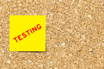 Yellow note paper with word testing on cork board background with copy space