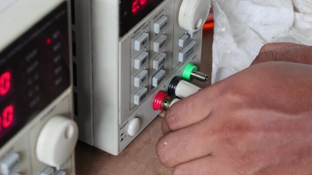 Hands connecting banana plugs to a laboratory DC power supply unit for testing and electronic troubleshooting.
