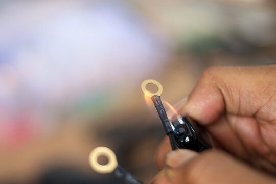 Close-up of a hand using a lighter to heat shrink insulation tubing over a crimped ring terminal on an electrical wire. - Powered by Adobe