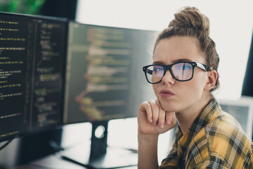 Young female software developer analyzing code on a dual monitor workspace in casual setting