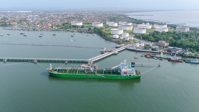 Aerial view of an oil tanker docked and conducting oil transfer operations near a coastal energy terminal. The scene illustrates potential environmental disaster risks and including oil spills.
