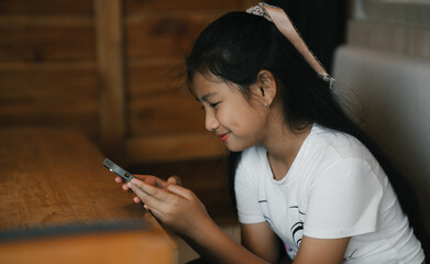 A young girl sits comfortably indoors,focused on her phone as warm light gently surrounds her.