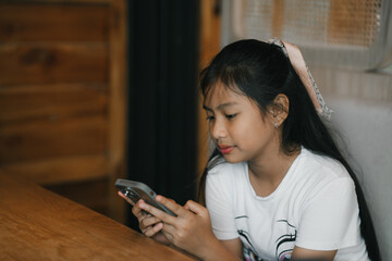 A young girl sits comfortably indoors,focused on her phone as warm light gently surrounds her.