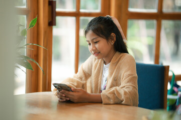 A young girl sits comfortably indoors,focused on her phone as warm light gently surrounds her.