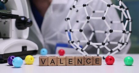 Chemist uses modern microscope at careful analysis. Word Valence formed from wooden blocks by molecular serves as visual reference for ongoing study