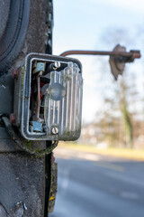Broken sidelight of an old army truck, with rust and moss over it, and a broken rearview mirror, during a sunshiny day, close to a street.