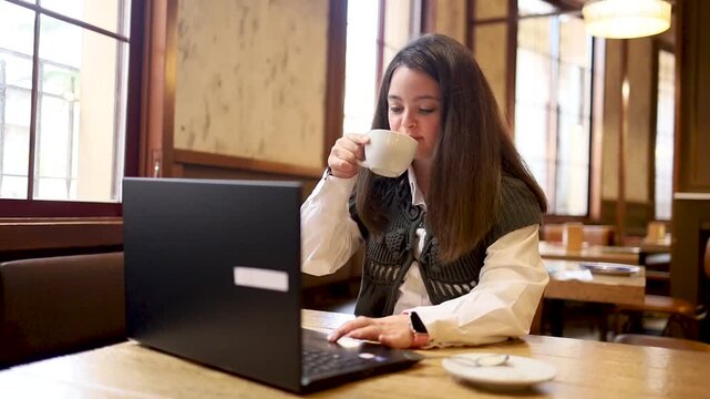 Video of a young girl with Down syndrome working on a laptop in a cafe.The girl is using the laptop while drinking coffee. Concept of trisomy 21.