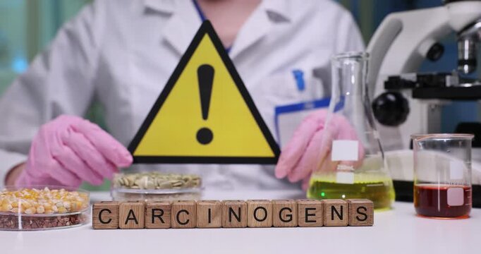 Lab worker shows warning sign to emphasize potential risks associated with ongoing experiment. Word Carcinogens formed from wooden blocks on table