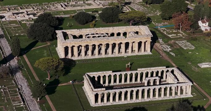 Aerial view of the weathered yet majestic Temples of Hera, standing as testaments to antiquity amidst the grassy landscape, Paestum, Campania, Italy.
