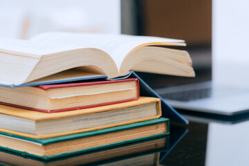 A stack of several books is placed on a table, with the top book left open