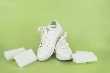 Still life of a pair of clean white sneakers and four rectangular white cleaning sponges against a solid light green background.