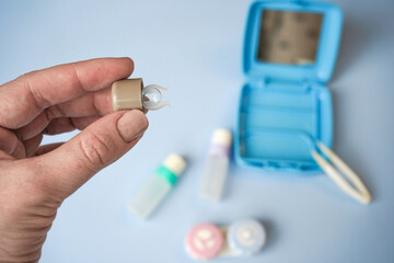 A close-up of a hand in a blue latex glove holding a contact lens with a small applicator.