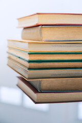 A stack of several books is placed on a table, with the top book left open