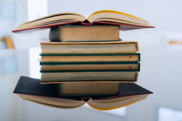 A stack of several books is placed on a table, with the top book left open