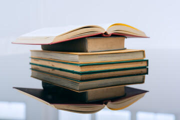 A stack of several books is placed on a table, with the top book left open