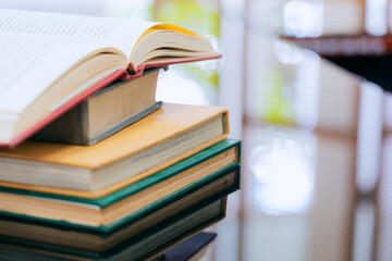 A stack of several books is placed on a table, with the top book left open