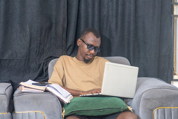 Male writing ideas in a notebook, surrounded by books and a laptop.