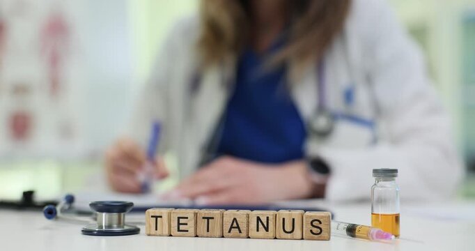 Wood blocks spell word Tetanus in clinic highlighting vaccine danger. Woman doctor writes note preparing immunization shot for patient at appointment