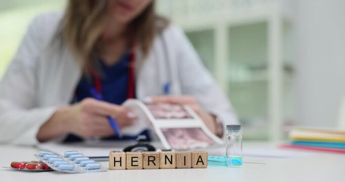 Wooden blocks spell word Hernia near syringe vial and pills by stethoscope. Woman doctor reads report planning detailed abdominal surgery assessment