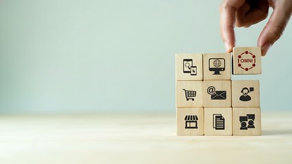A hand delicately places a cube bearing an eye icon atop a foundation of blocks etched with an array of symbols signifying various technologies, subtly alluding to business.