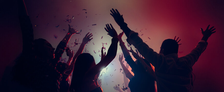 Crowd celebrating with raised hands and falling confetti. Concept of Christmas holiday climax, shared emotions, nightlife energy, festive unity and joyful event promotion visuals. Banner