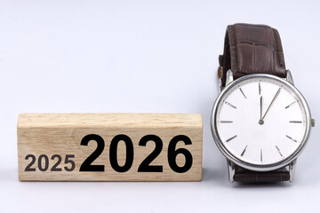 An analog clock showing five  minutes past twelve next to a block with the inscription &ldquo;2025 and 2026,&rdquo; symbolizing the New Year change, resolutions, the passage of time, and delays.