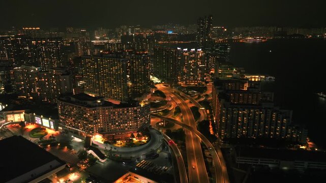 Aerial view of brightly lit buildings interspersed with roads and highways, creating a vibrant tapestry of light against the dark sky, Kowloon, Hong Kong.