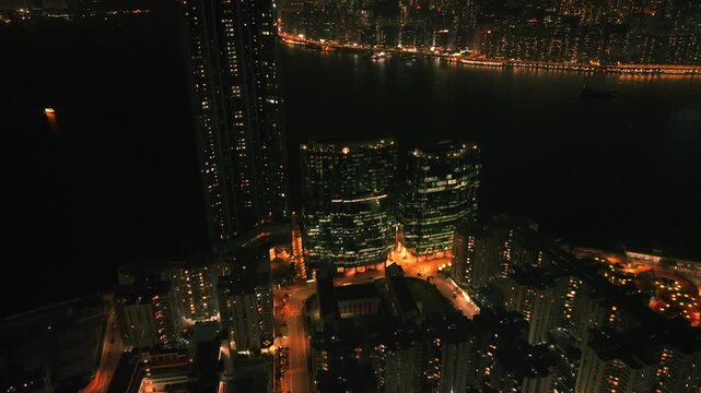 Aerial view of illuminated buildings at night showcase a vibrant urban landscape with bright lights reflecting on the dark waters, Kowloon, Kowloon, Hong Kong.