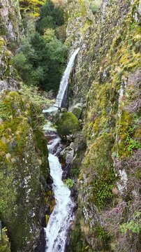 Aerial view of the Poco do Inferno waterfall cascading down the rocky cliffs, surrounded by green vegetation, Poco do Inferno, Manteigas, Portugal.
