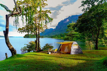 Camping tent on green grass in the morning, antique gas lamps, retro chairs, with outdoor coffee-making facilities on tables in a forest camping area.
