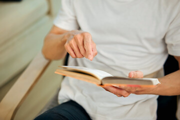 Closeup man relaxes in a armchair at home while reading a book in a cozy living room