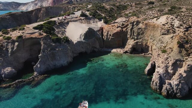 Aerial view of the beach nestled between towering cliffs where people gather near the clear blue water, creating a striking contrast, Milos, Tsigrado beach, Greece.