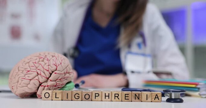 Woman psychiatrist writes sequence of therapeutic steps for managing oligophrenia. Wooden blocks forming diagnosis Oligophrenia arranged on table