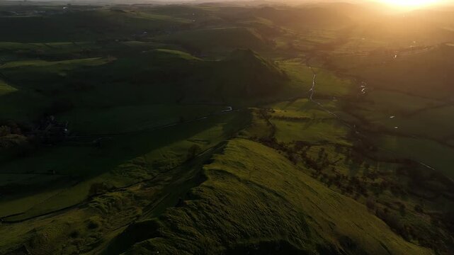 Aerial view of the undulating green hills and valleys bathed in golden sunlight creating stark shadows, Buxton, England, United Kingdom.