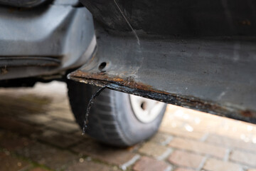 Rust and corrosion damage on the bottom edge of a car's left side door. Close up, low, wide angle view, no people