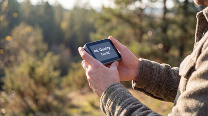 Person checking portable air quality monitor device showing good reading outdoors in natural forest environment for pollution measurement atmospheric health safety and environmental awareness monitor