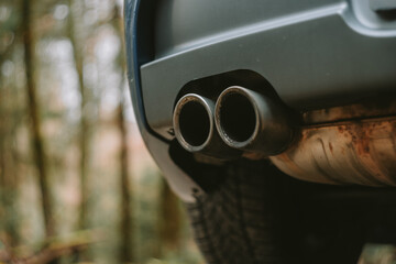 Generic car twin exhaust or tail pipe tips. Close up, ground level shot, no people, blurry forest background