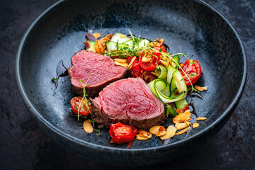 Fine dry aged beef filet steak rare tataki style cut tagliata with sliced zucchini, tomato and almonds served as close-up on a design plate