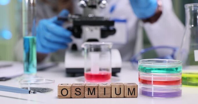 Woman lab worker observes microscopic details of substance. Wooden cubes form word Osmium clearly indicating chemical element under investigation
