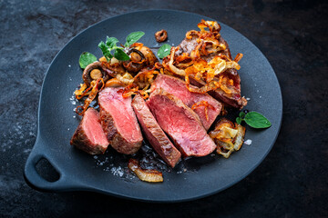 Zwiebelrostbraten roast beef - sirloin beef steak braised with fried onion rings and mushrooms served as close-up on a deisgn plate