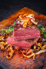 Zwiebelrostbraten roast beef - sirloin beef steak braised with fried onion rings served as close-up on the old wooden cutting board