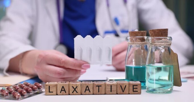 Doctor holds pack of medical suppositories and explains purpose. Wooden blocks arranged to form word Laxative highlight prescribed medication