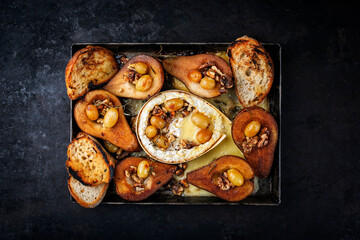 Oven baked camembert cheese with caramelized glazed pears, walnuts and grapes and baguette served as top view on a rustic backing form