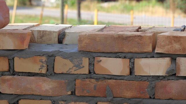 Professional construction worker is laying bricks while building a wall at a construction site. Close up of bricklayer using masonry tools to apply mortar and align the bricks with precision.