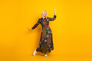 Elegant mature woman in a patchwork dress poses joyfully against a bright yellow background for stock advertising