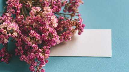 Pink dried flowers rest beside a blank, white card on a teal background