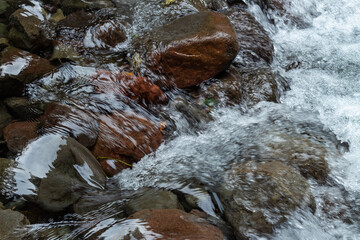 Close up fresh waterfall stream rushing over wet brown river rocks texture in a natural setting.