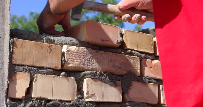 Professional construction worker is laying bricks while building a wall at a construction site. Close up of bricklayer using masonry tools to apply mortar and align the bricks with precision.