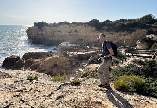 Male photographer with backpack and camera walks coastal trail, Arco de Albandeira, Praia da Estaquinha